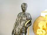 a statue of a woman holding a book next to a vase of flowers