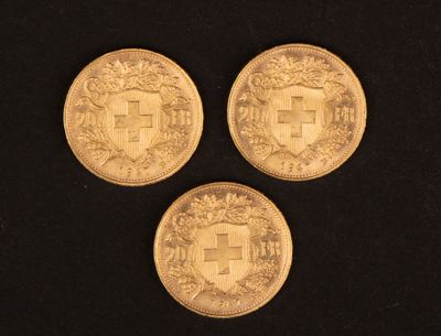 trois pièces d'or posées sur une surface noire, sur fond noir
