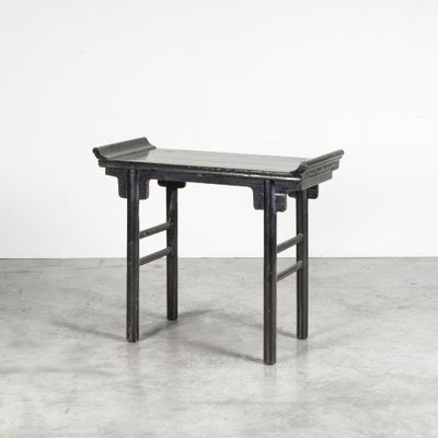 une table en bois noir avec un plateau en verre, posée sur un sol en béton