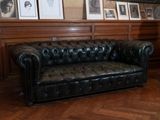 un canapé en cuir noir dans une pièce où sont accrochés des tableaux aux murs