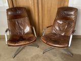 pair of brown leather lounge chairs with chrome legs and arms