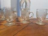 four cups and a jug sitting on a wooden table