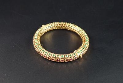 un gros plan sur un bracelet en or orné de pierres vertes et rouges