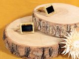 pair of black and gold cufflinks on a tree slice with a flower