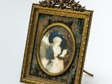 an old picture of a woman in a blue hat is hanging on a gold frame