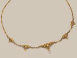 a close up of a gold necklace with pearls on it