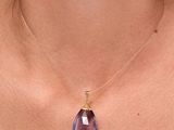 un gros plan d'une femme portant un collier orné d'une pierre violette