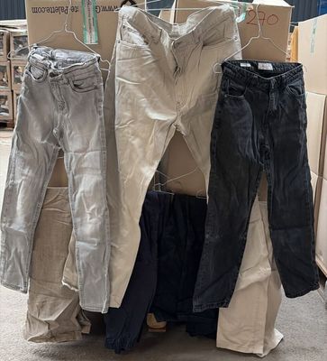 Plusieurs paires de jeans sont empilées sur des cartons dans un entrepôt