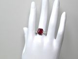une image représentant la main d'une femme tenant une bague sertie d'une pierre rouge