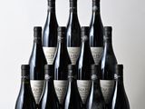 six bottles of wine sit on a wooden table in front of a white wall
