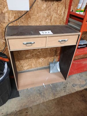a wooden desk with drawers and a trash can in the corner
