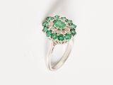 a close up of a ring with green stones on a white surface