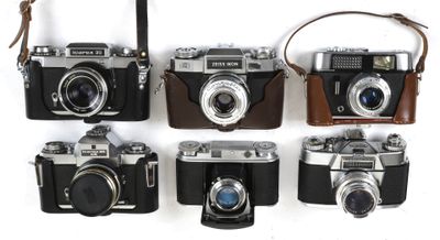 four old cameras are lined up on a white surface