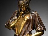 a bronze statue of a woman in a dress holding her hands to her face