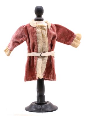 une poupée vêtue d'un manteau rouge et d'une écharpe blanche, posée sur un mannequin noir