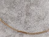 a gold necklace with a curved bar on a chain