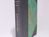 an old book with a green cover sitting on top of a white surface