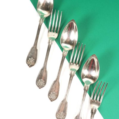 cinq cuillères en argent et deux fourchettes en argent sur un fond vert et blanc
