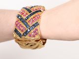 someone is wearing a gold bracelet with blue and pink stones on it
