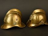 pair of brass fire helmets on a black background