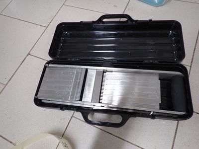 une mallette noire posée par terre, dans laquelle se trouve un couteau