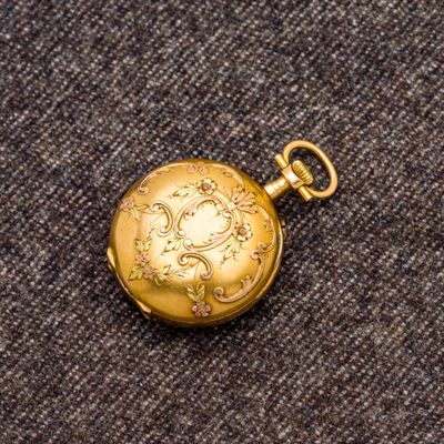 une image représentant une montre de poche en or posée sur un tapis