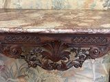 une table au plateau en marbre et au piètement en bois, posée devant un mur recouvert de papier peint à motifs floraux