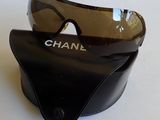 des lunettes de soleil Chanel posées sur un étui noir, sur une surface blanche