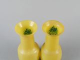 pair of yellow vases with green flowers in them sitting on a table