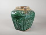 a green vase with a gold lid sitting on a white surface
