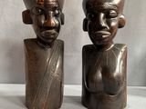 deux statues en bois représentant un homme et une femme, posées sur une surface blanche