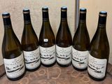 six bottles of wine are lined up on a wooden barrel