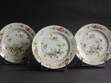 three plates with floral designs are on a stand against a black background
