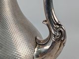 a silver tea pot with a handle on a table