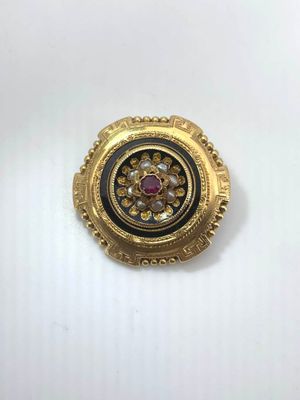 a close up of a gold and black broochle on a white surface