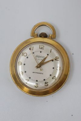 a gold pocket watch with a white face on a white surface