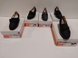 Quatre paires de chaussures noires sont exposées dans une vitrine.