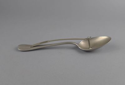 un gros plan d'une cuillère en argent avec un manche, posée sur une surface grise