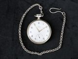 une montre de poche en argent attachée à une chaîne, posée sur une surface noire