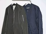two jackets hanging on a clothes rack against a white wall