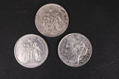 trois pièces d'argent posées sur une surface noire, sur fond noir