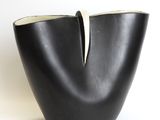 a black vase with a white handle sitting on a white surface