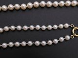 a white pearl necklace with a gold clasp on a black background