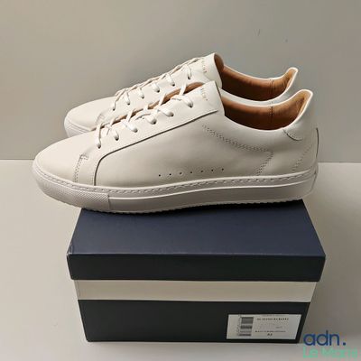 Les baskets blanches sont posées sur une boîte bleue.