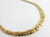 le collier en or est posé sur une surface blanche, devant un fond blanc