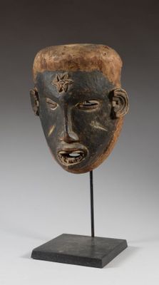 un masque en bois au visage noir, posé sur un socle