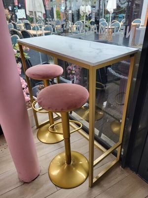des tabourets de bar roses et dorés et une table au plateau en marbre devant une fenêtre