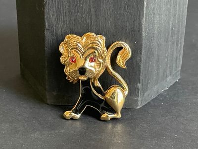 a gold lion brooch with a red stone in the background