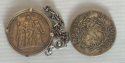 deux pièces d'argent sont posées sur une chaîne, sur une surface blanche