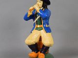 figurine représentant un homme vêtu d'un manteau bleu et d'un chapeau, jouant de la flûte